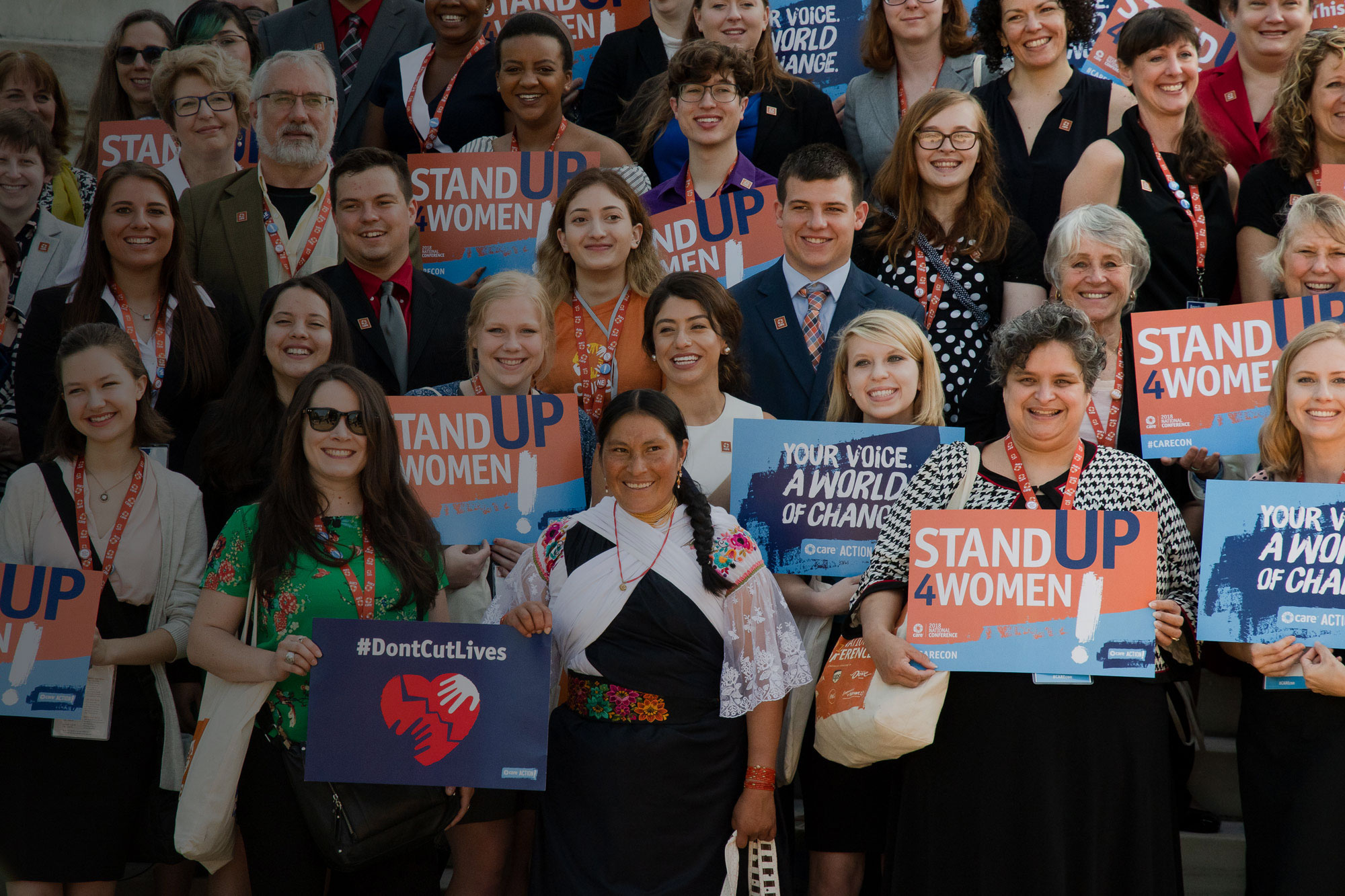 A large group of people stand on steps holding CARE Action signs.