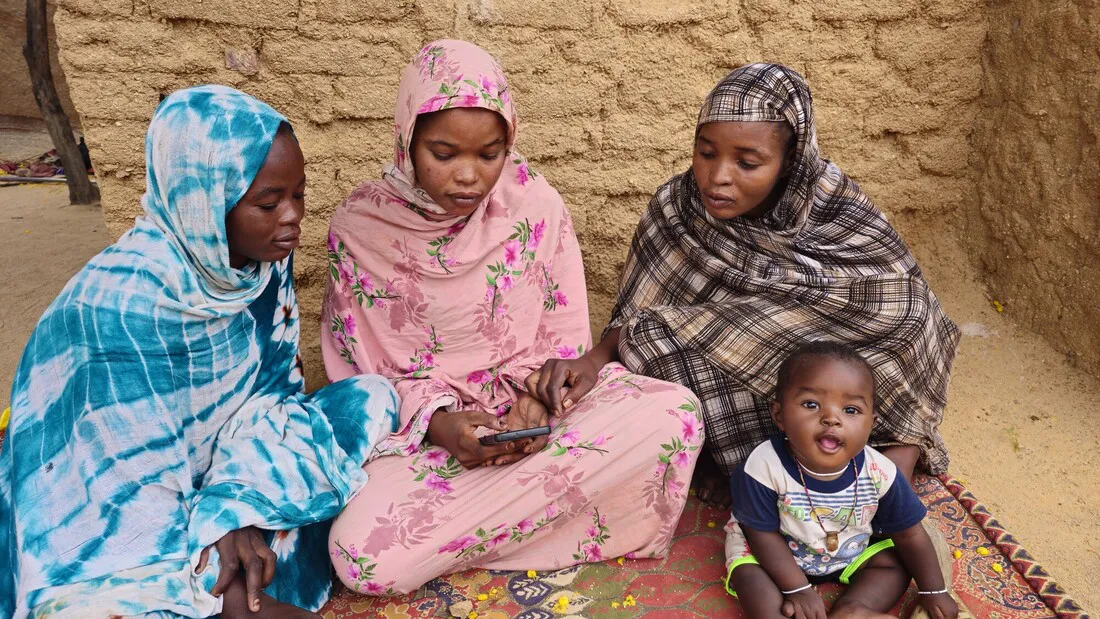 Three Sudanese women sit together with a young child.